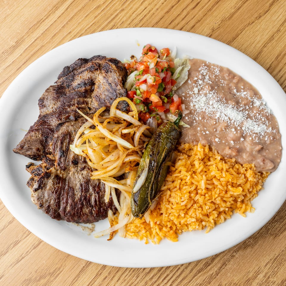 Grilled steak platter with sautéed onions, roasted pepper, pico de gallo, Mexican rice, lettuce, and refried beans.