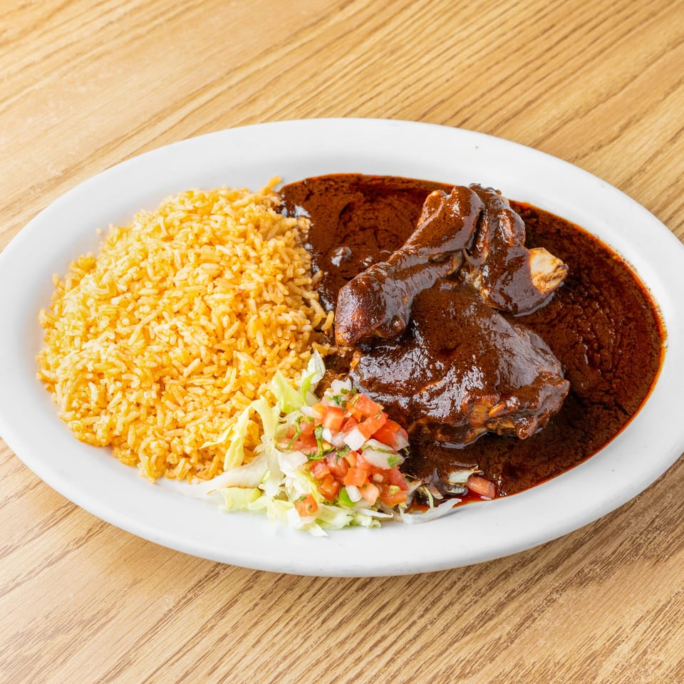 Plate of yellow rice, braised meat in rich brown sauce, and fresh lettuce and tomato salad on a wooden table.